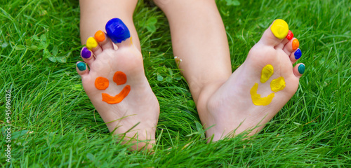 Children's feet with a pattern of paints smile on the green grass. Selective focus. © Anna