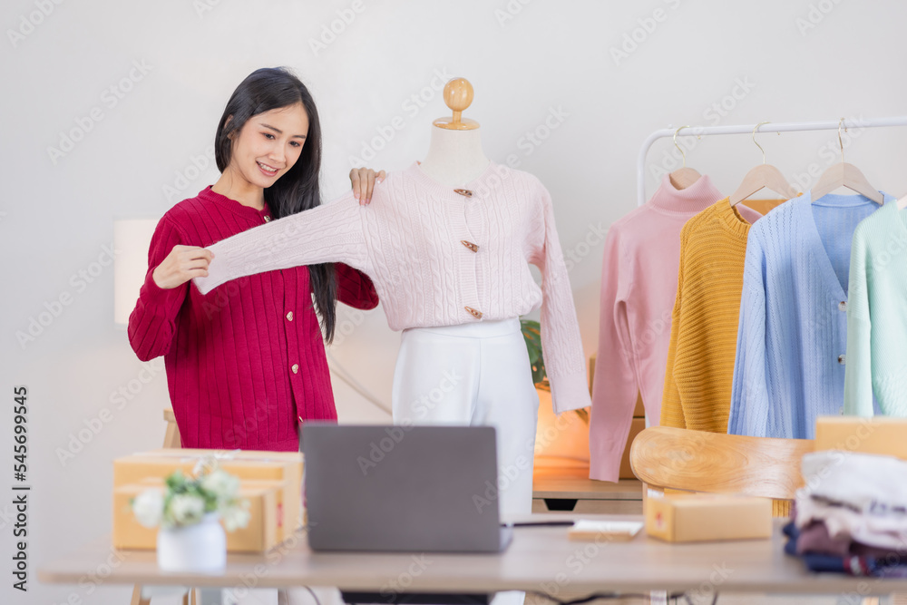 Asian women SME selling clothes online, She is answering customers' questions by phone and laptop at home, Starting Small business entrepreneur freelance, Online business, SME concept. Asian women SME selling clothes online, She is answering customers' questions by phone and laptop at home, Starting Small business entrepreneur freelance, Online business, SME concept.