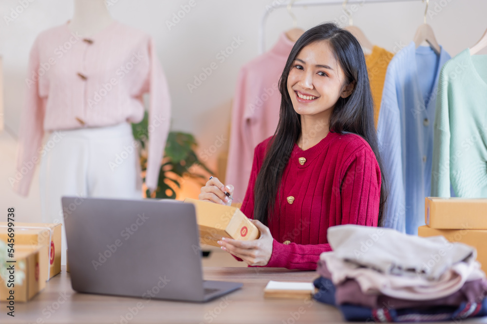 Fototapeta premium Asian women SME selling clothes online, She is answering customers' questions by phone and laptop at home, Starting Small business entrepreneur freelance, Online business, SME concept.