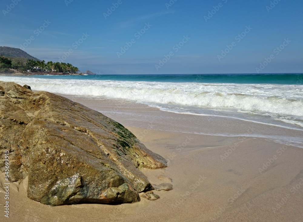 Beautiful view of foamy waves crashing on a sandy beach, on a sunny day, and a big rock at the beach Beautiful view of foamy waves crashing on a sandy beach, on a sunny day, and a big rock at the beach