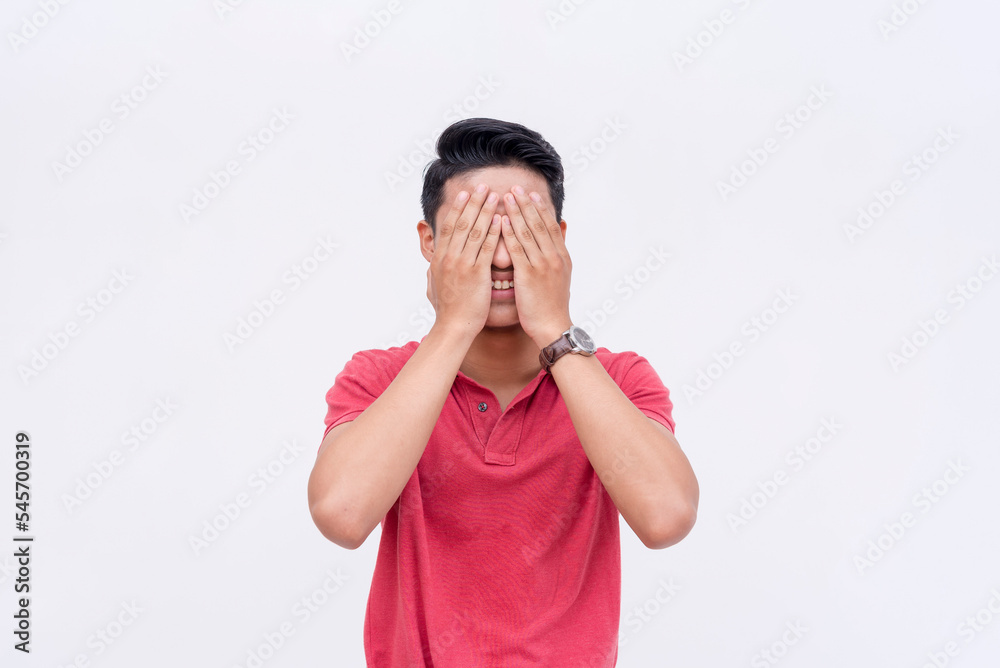 A young asian man covers her eyes with her hands while smiling. Excited and anticipating a happy surprise. Isolated on a white background. Spoiler alert concept. A young asian man covers her eyes with her hands while smiling. Excited and anticipating a happy surprise. Isolated on a white background. Spoiler alert concept.