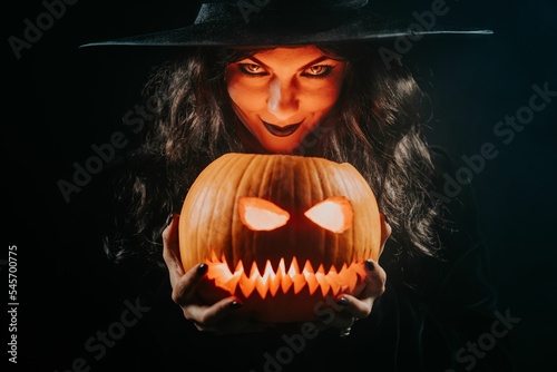 Mysterious black witch with pumpkin as head of jack-o-lantern on dark