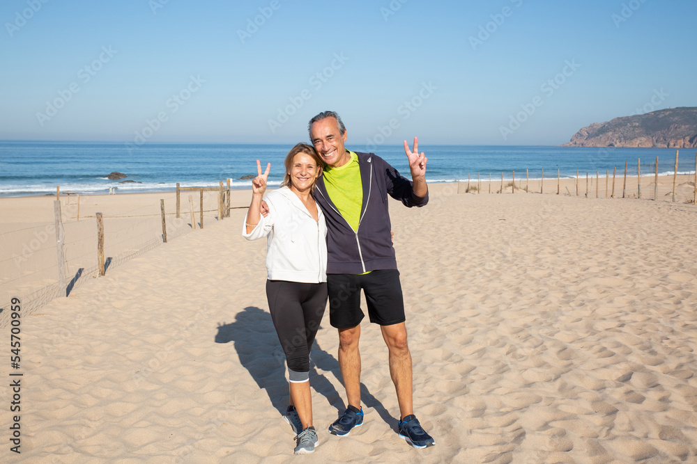 Portrait of senior couple posing for camera after training. Caucasian man and woman full of vigor after jogging hugging and showing victory gesture for camera. Healthy lifestyle of aged people concept Portrait of senior couple posing for camera after training. Caucasian man and woman full of vigor after jogging hugging and showing victory gesture for camera. Healthy lifestyle of aged people concept