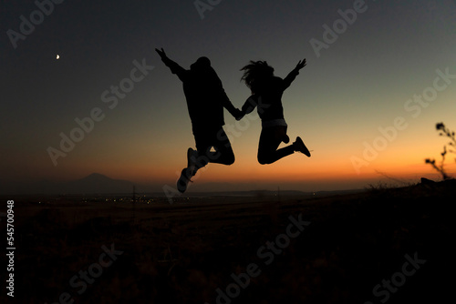 Silhouette of a couple jumping against the sky during sunset