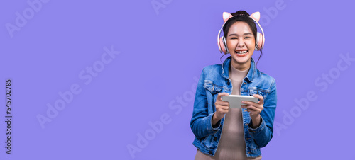 Beautiful Asian young woman in jacket jean and playing video games using joysticks with headphones on voilet background isolated. © anon