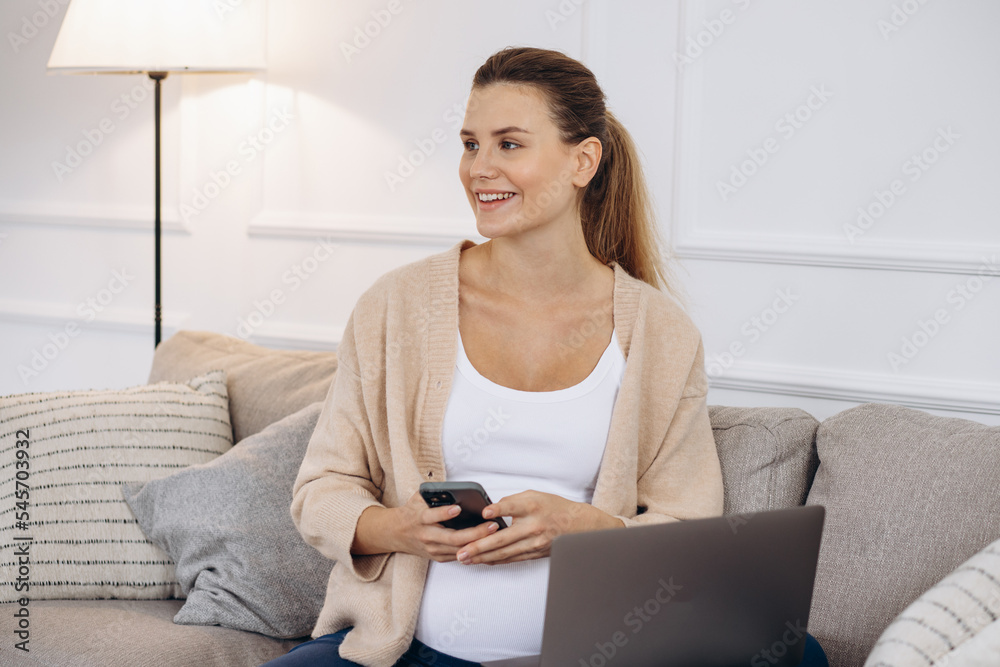 Pregnant woman sitting on coach using laptop and holding headphons by the belly Pregnant woman sitting on coach using laptop and holding headphons by the belly