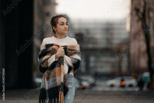 Happy young adult woman smiling with teeth smile outdoors and walking on city street weating winter clothes and knitted scarf. Female young traveler in Warsaw, Poland.