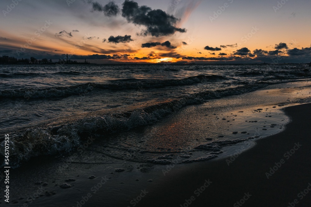 Scenic view of ocean waves crashing against the beach at a cloudy sunset