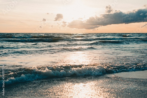 Φωτογραφία Scenic view of ocean waves crashing against the beach at a cloudy sunset