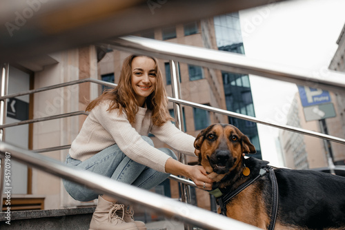 Pretty woman have outdoor near office building with her big dog while sitting on the stairs, hugs her dog. Pet friendly and pet care concept. Animal lover.
