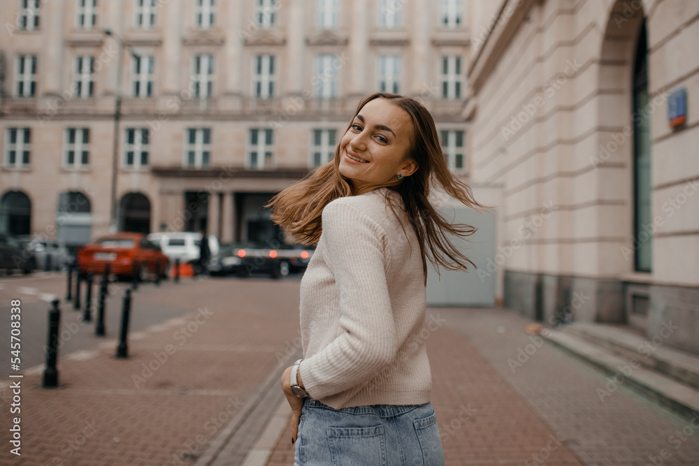 Close-up portrait of laughing brunette girl in beige sweater on city background. Woman posing.