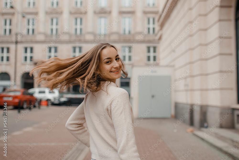 Close-up portrait of laughing brunette girl in beige sweater on city background. Woman posing.