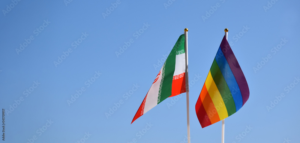 Iran national flag and rainbow flag stand together against bluesky background, concept for lgbt celebration and respecting gender diversity of human in Iran, soft and selective focus.