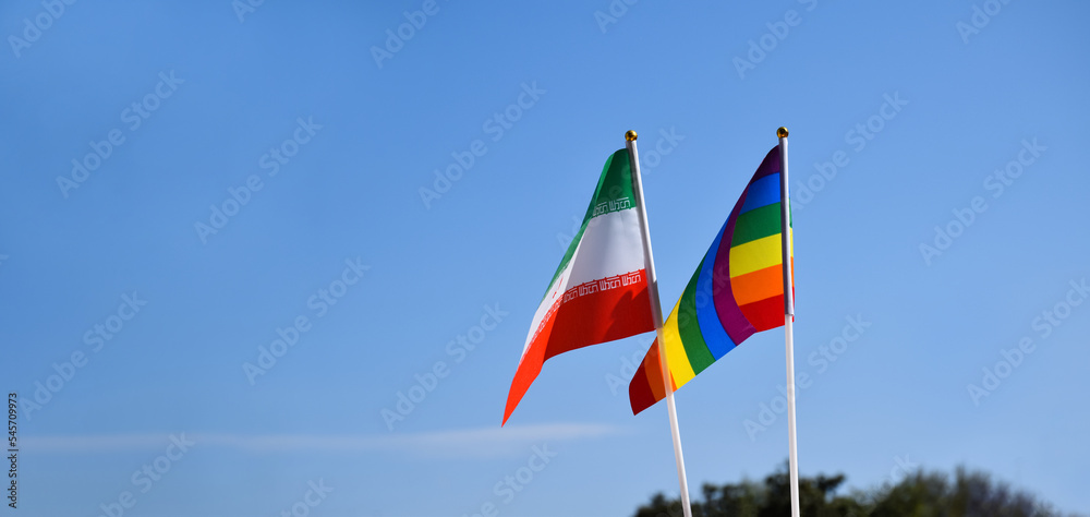 Iran national flag and rainbow flag stand together against bluesky background, concept for lgbt celebration and respecting gender diversity of human in Iran, soft and selective focus. Iran national flag and rainbow flag stand together against bluesky background, concept for lgbt celebration and respecting gender diversity of human in Iran, soft and selective focus.