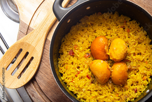 Uma panela preta com arroz com pequi e uma colher de madeira, sobre uma tábua de cozinha. Um prato típico brasileiro. photo