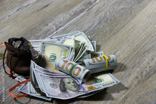 Closeup of one hundred dollar bills of American dollars and a money sack with different coins of the world on a gray wooden table