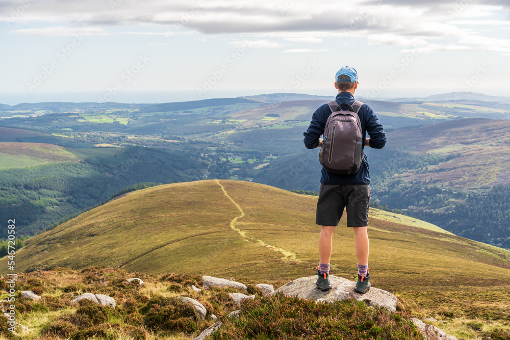 Valokuva Hiker standing on a mountain peak looking at the path leading down