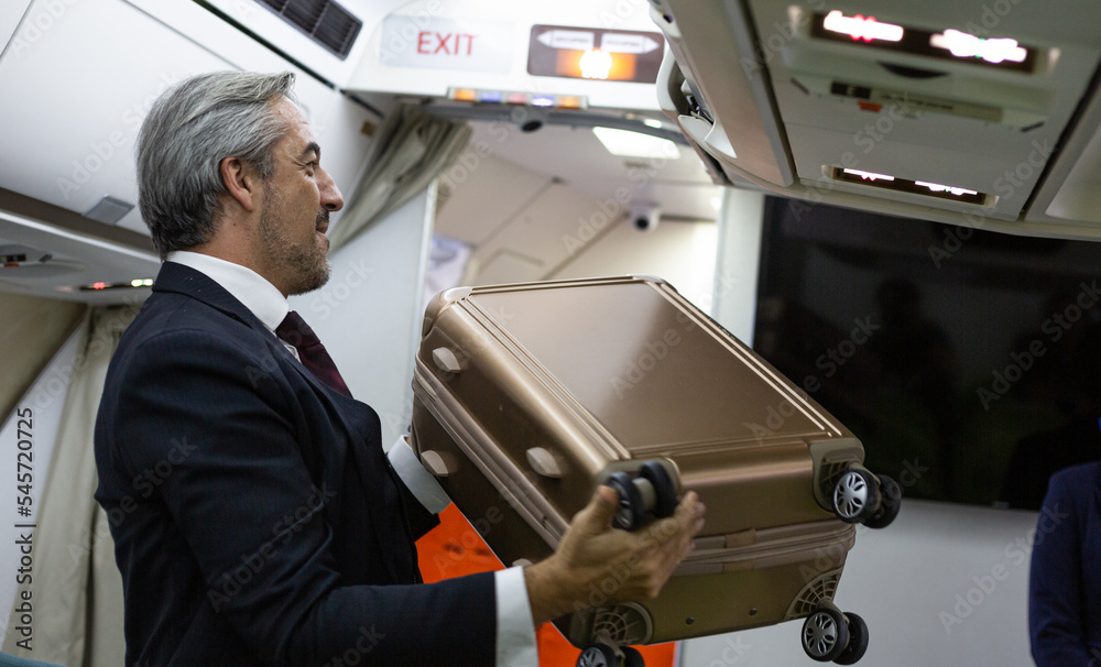 Caucasian business man put cabin luggage into the airplane storage before flight departure