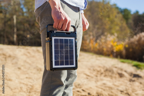 A guy carries a portable solar panel for charging equipment. The model is holding a portable battery for nature. photo