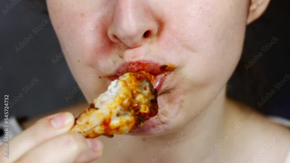 Woman eating a takeaway fried chicken wing from fast food cafe with a mouth and teeth close up Woman eating a takeaway fried chicken wing from fast food cafe with a mouth and teeth close up