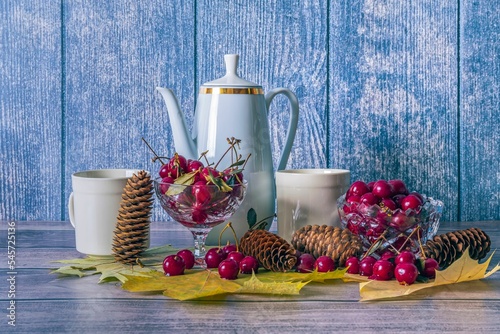 Festive still life with white teapot and mugs for drinks, ripe red cherries on wooden surface.