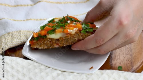 A hand put a homemade Low-Carb Keto Meatza (grain and gluten free beef meat-based pizza) slice with vegetables and mozzarella cheese on a white plate on wooden background close up photo