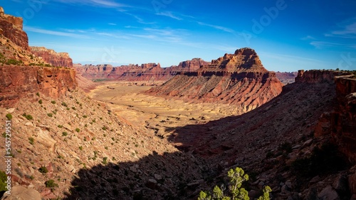 Scenic shot of a red desert valley with cliffs and peaks with the blue sky in the background