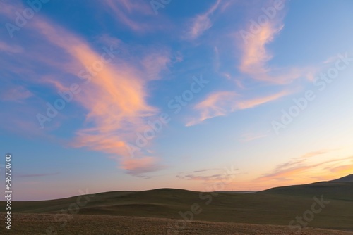 Fotografia Sunrise view over the landscape with purple, sunlit clouds over the grassland
