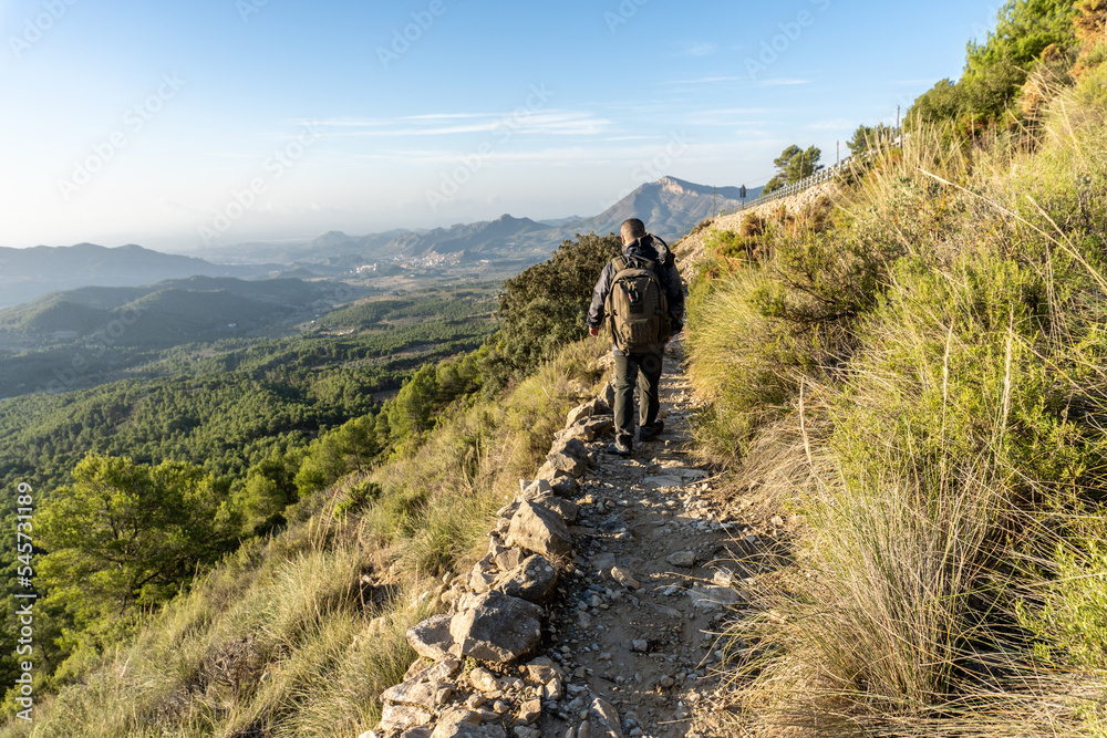 Rear view, man with a backpack is hiking on a rocky path