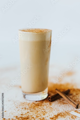 Closeup shot of a glass of a cinnamon mocha shake, surrounded with cinnamon sticks and powder