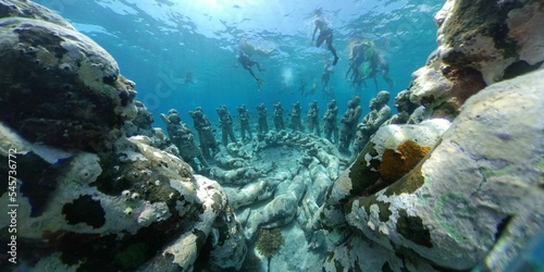 Underwater scenery with sunk old sculptures covered in moss and people scuba diving