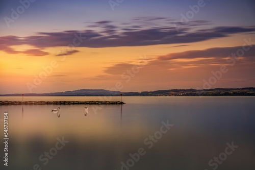 Beautiful sunset scene over large sea with ducks and land on the horizon