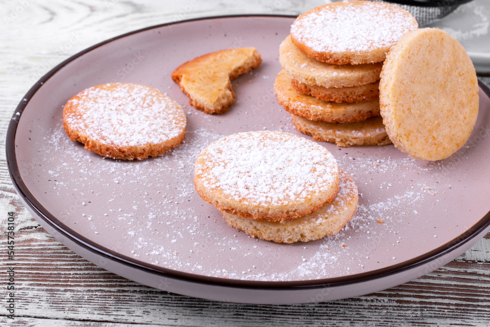 Shortbread cookies of round shape covered with sugar powder on the plate. 