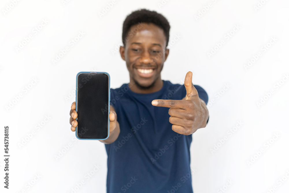 Happy man showing phone screen. Young African American male model in blue T-shirt pointing at smartphone screen, presenting product. Portrait, studio shot, technology, advertising concept Happy man showing phone screen. Young African American male model in blue T-shirt pointing at smartphone screen, presenting product. Portrait, studio shot, technology, advertising concept