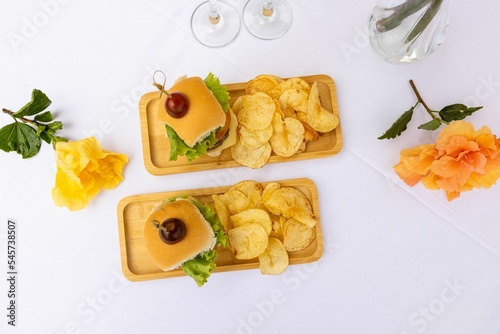 Top closeup of burger and chips on the wooden plates, two glasses full of champagne