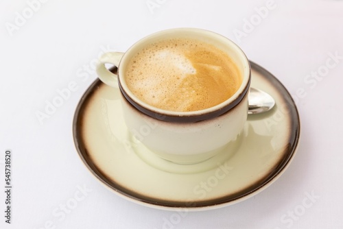 Top closeup of a cup of cappuccino on a plate with brown edges and a little spoon near
