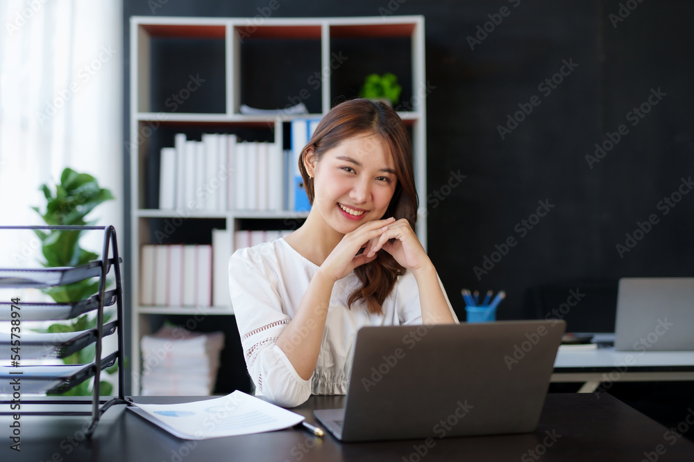 Attractive young Asian businesswoman using laptop in office smiling and looking at camera. Attractive young Asian businesswoman using laptop in office smiling and looking at camera.