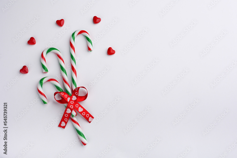 Candy canes of red-green color, red heart shaped candies, red ribbon in the shape of a bow, light background Candy canes of red-green color, red heart shaped candies, red ribbon in the shape of a bow, light background