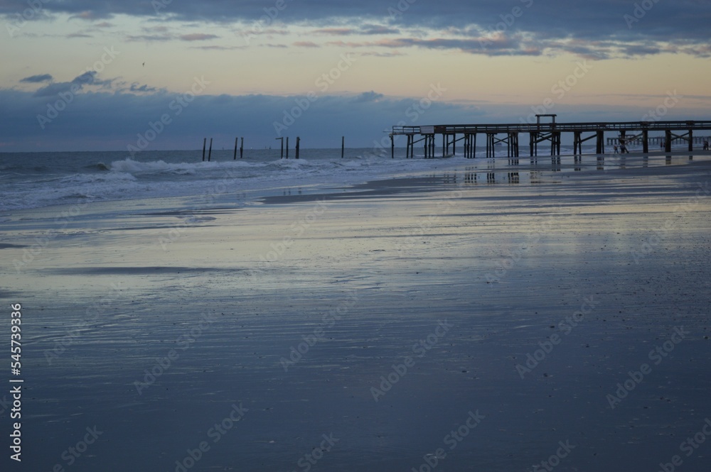 Calm seascape with a pier and splashing waves at soft sunset