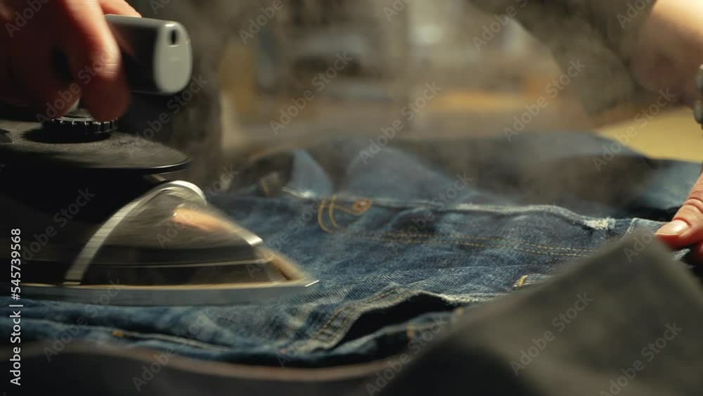 A female tailor seamstress ironing jeans before repair in a workshop repairing old denim clothes. Small family business, tailoring and repair of clothes, handmade, couturier, tradition A female tailor seamstress ironing jeans before repair in a workshop repairing old denim clothes. Small family business, tailoring and repair of clothes, handmade, couturier, tradition