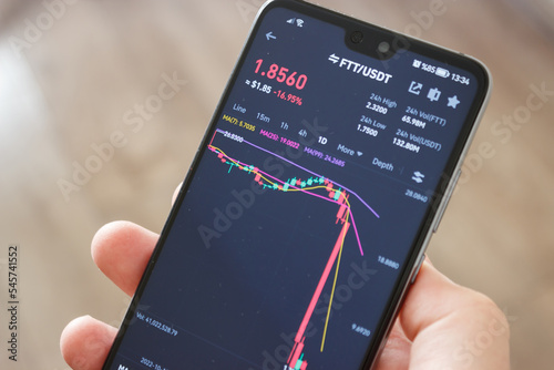 FTT coin is losing value. Exchange went bankrupt. Man holding smartphone on hand with FTT graph screen. FTT coin crash. photo