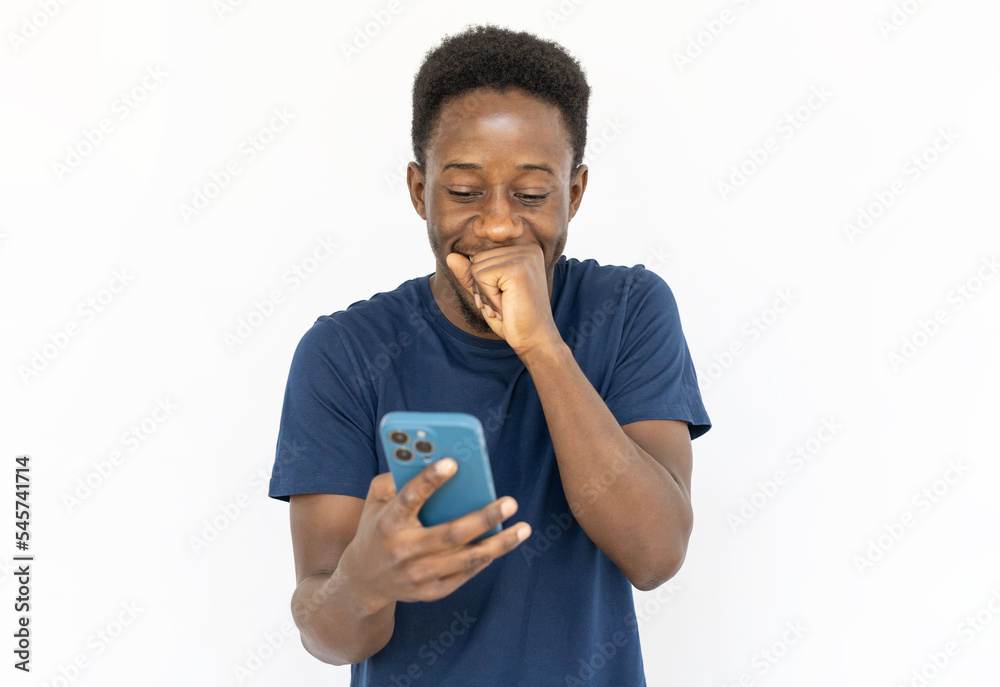 Surprised man covering mouth with clenched fist. Young African American male model in blue T-shirt looking at smartphone with joy. Portrait, studio shot, technology, joy concept Surprised man covering mouth with clenched fist. Young African American male model in blue T-shirt looking at smartphone with joy. Portrait, studio shot, technology, joy concept