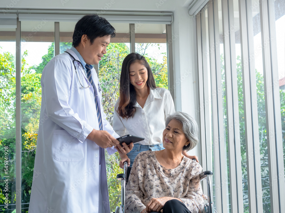 Obraz premium Happy senior woman patients in wheelchair with grandchild take her to meet doctor male use tablet discussing her medical treatment records in hospital. Senior adult checkup appointment concept.