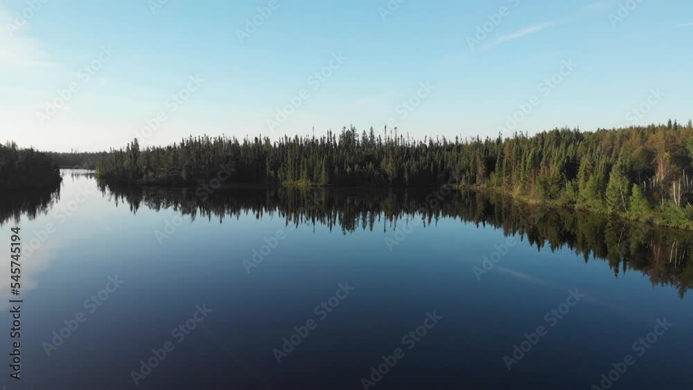 Drone moving sideways over a very calm boreal lake that is surrounded by forest. The still water is reflecting the clear blue sky
Drone moving sideways over a very calm boreal lake that is surrounded by forest. The still water is reflecting the clear blue sky