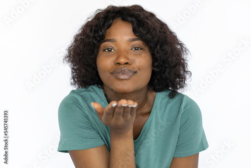 Attractive young woman showing kiss gesture. Beautiful African American female model in blue T-shirt blowing air kiss at camera. Studio shoot, emotion, love, relationship concept