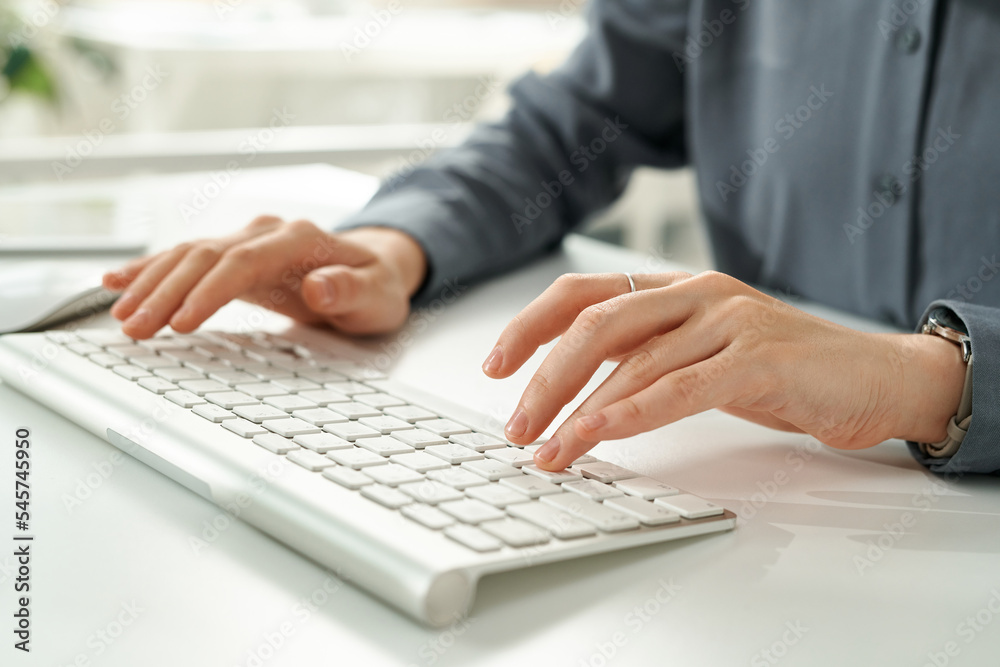 Close-up of young businesswoman typing on computer keyboard while sitting at table at office Close-up of young businesswoman typing on computer keyboard while sitting at table at office