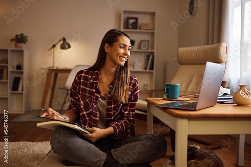 Young happy woman taking notes while studying online over laptop at home.