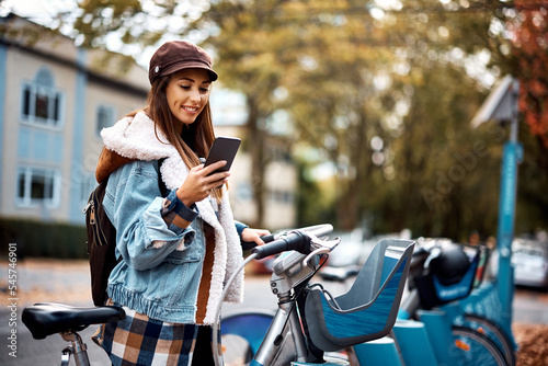 Young happy woman using smart phone while renting bike in city.