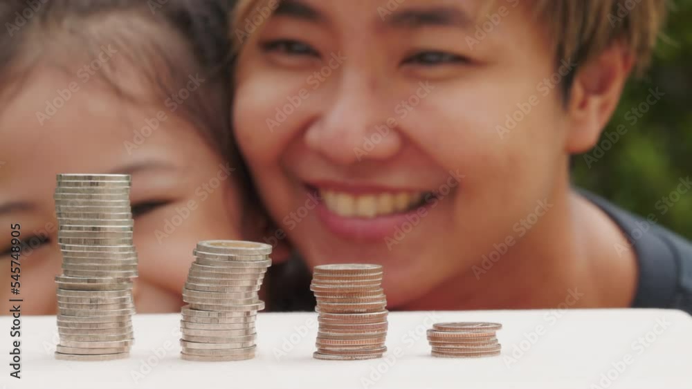 Closed up coin towers and cheerful asian mother and daughter who is saving her money shows concept of financial planning and investment strategy for child future which is the success of wealthy. Closed up coin towers and cheerful asian mother and daughter who is saving her money shows concept of financial planning and investment strategy for child future which is the success of wealthy.