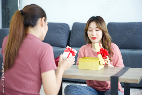 young woman smiling and opening a gift box with her friend on a table